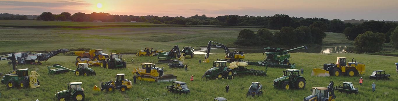 Menschen, die zwischen unterschiedlichen Arten von Ausrüstung von John Deere auf einem großen Feld umhergehen.