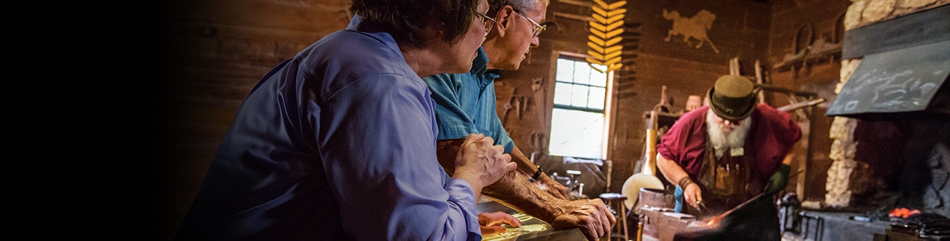 Ein älteres Ehepaar beobachtet den Schmied, der mit einem Metallhammer an der historischen Stätte in Grand Detour, Illinois, USA arbeitet