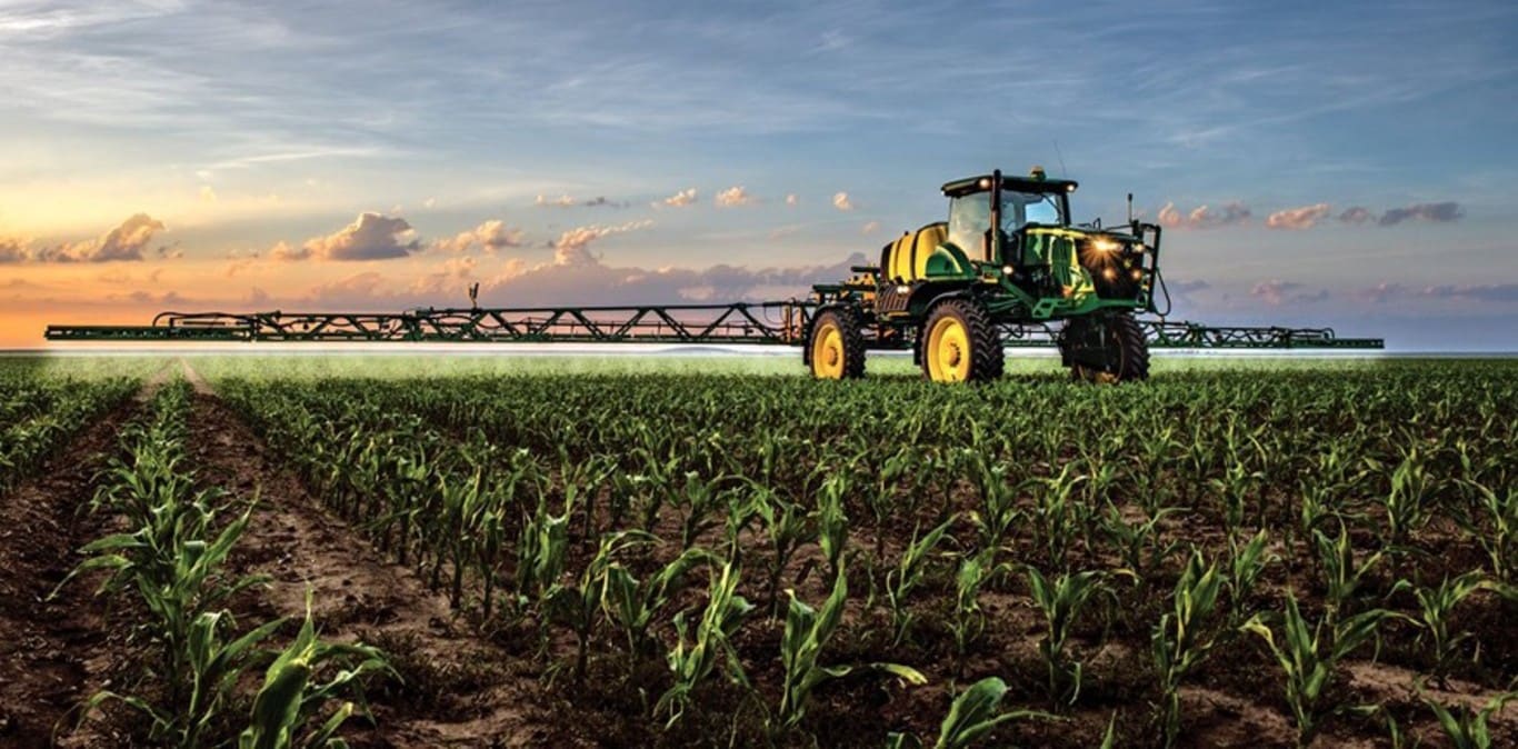 John Deere Feldspritze im Einsatz in einem Maisfeld vor untergehender Sonne