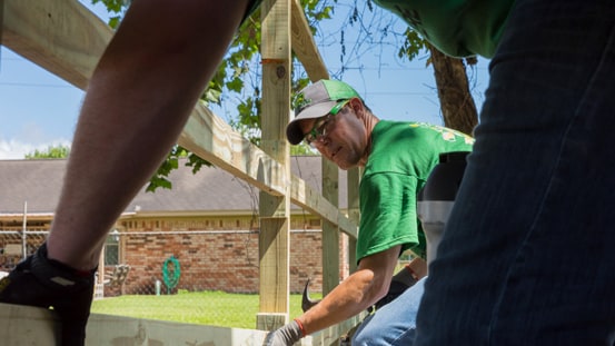 Zwei Menschen, die zusammen einen Zaun in der Nähe eines Gebäudes bauen.