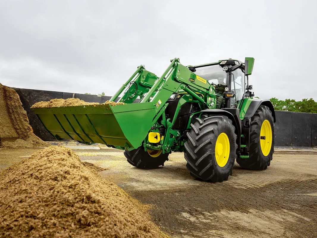 Mit Silage gefüllte Frontladerschaufel an einem John Deere Traktor während der Materialhandhabung.