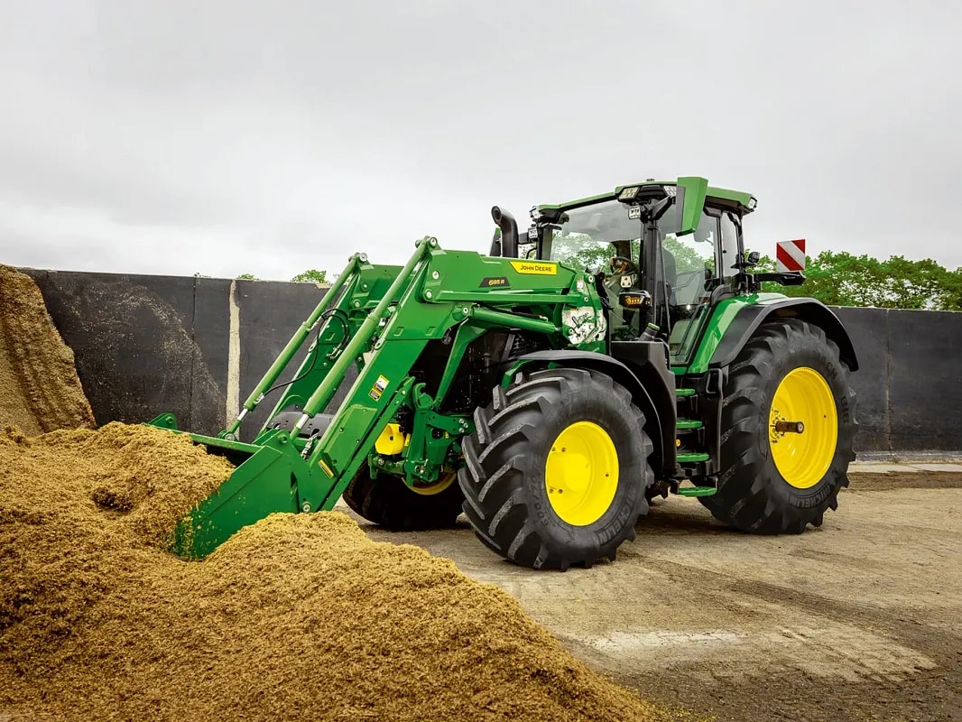 Ein John Deere Traktor schiebt seine Frontladerschaufel auf einem Hof in einen Silagehaufen.