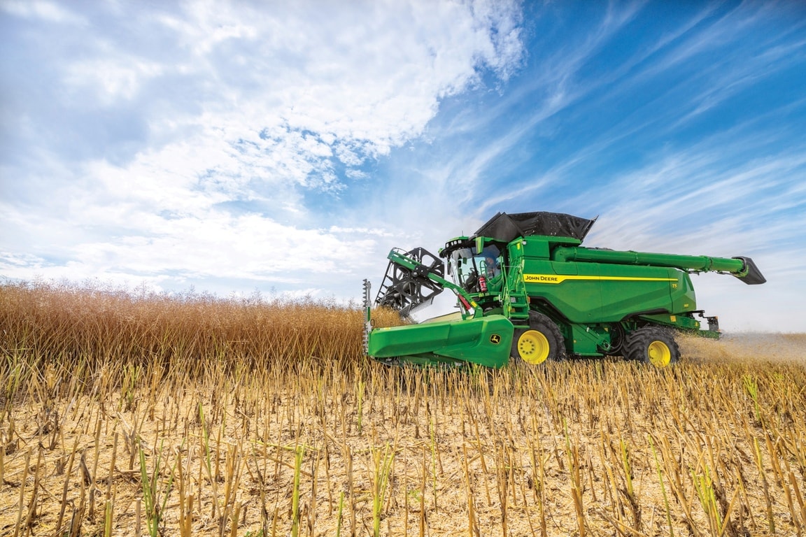 John Deere Mähdrescher erntet Getreide mit Erntevorsatz auf einem Feld unter blauem Himmel während der Getreideernte