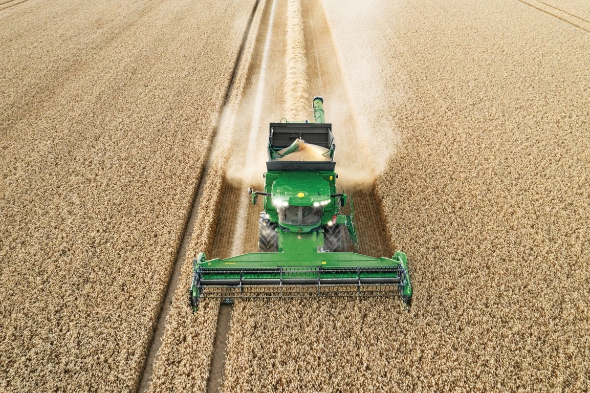 Mähdrescher entlädt Getreide während der Weizenernte, während der Erntevorsatz effizient arbeitet