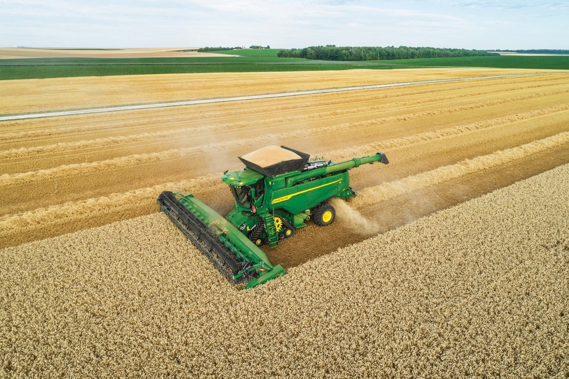 Luftaufnahme des Mähdreschers bei der Weizenernte über Feldern mit Streifenmuster, die großflächige Landwirtschaftsmuster zeigen