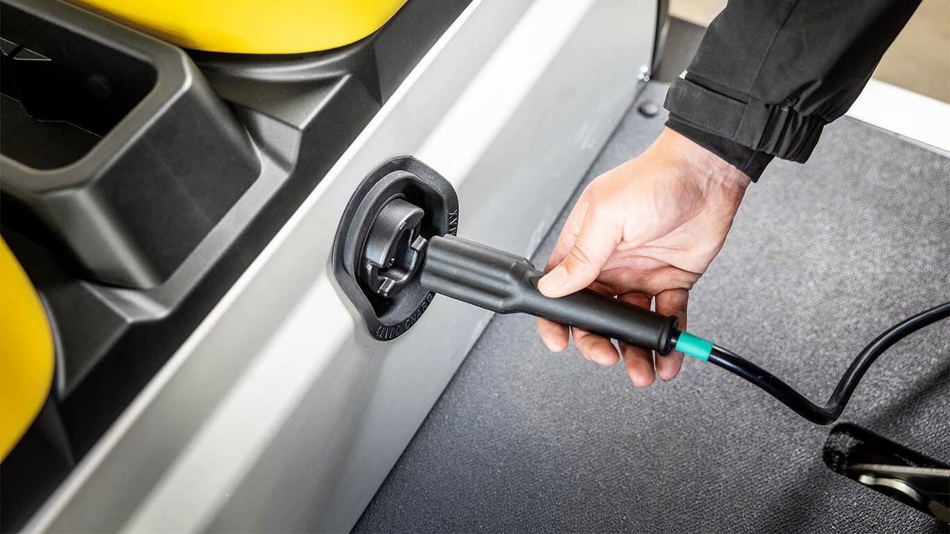Eine Hand steckt ein Ladekabel in den Seitenanschluss eines John Deere Gator GS Electric Nutzfahrzeugs.