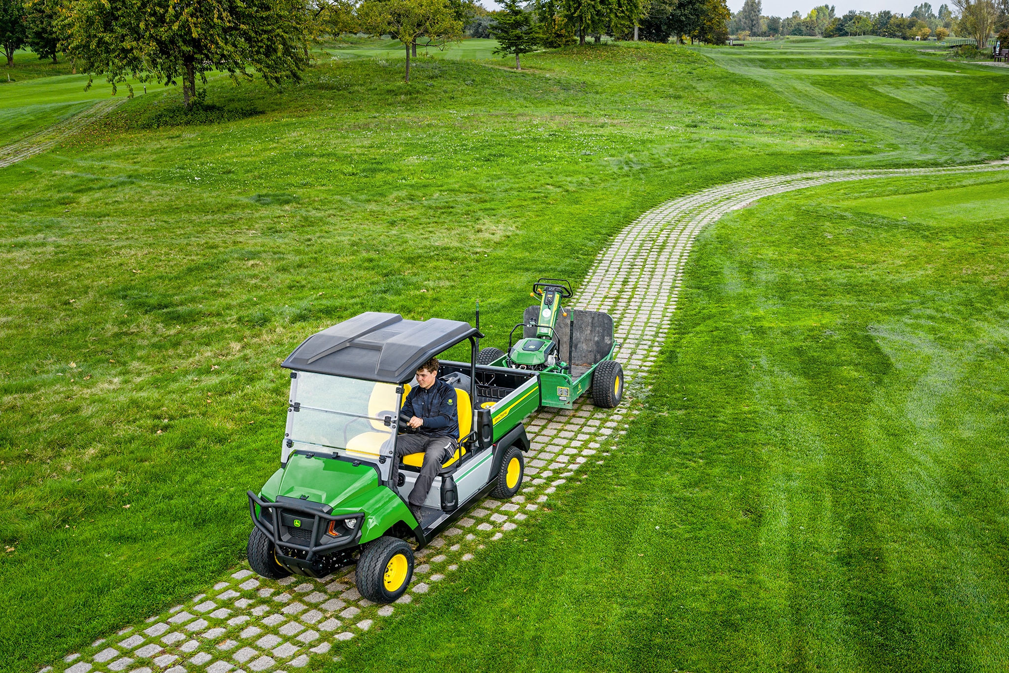 John Deere Gator GS zieht Geräte auf einem grasbewachsenen Weg eines Golfplatzes John Deere Gator GS zieht Geräte auf einem grasbewachsenen Weg eines Golfplatzes
