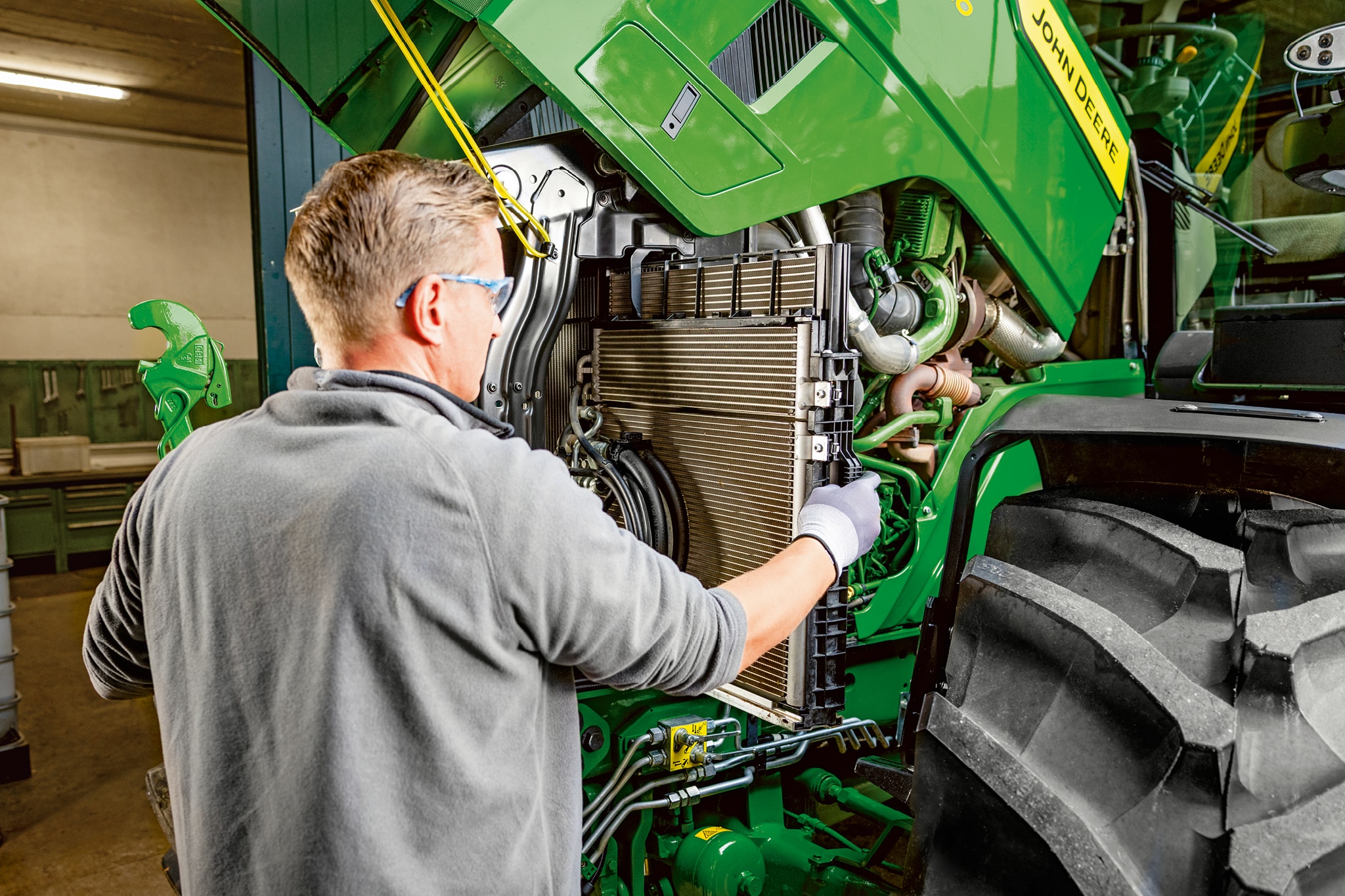 Un technicien effectuant des travaux d’entretien dans le compartiment moteur d’un tracteur John Deere de la série 6M.