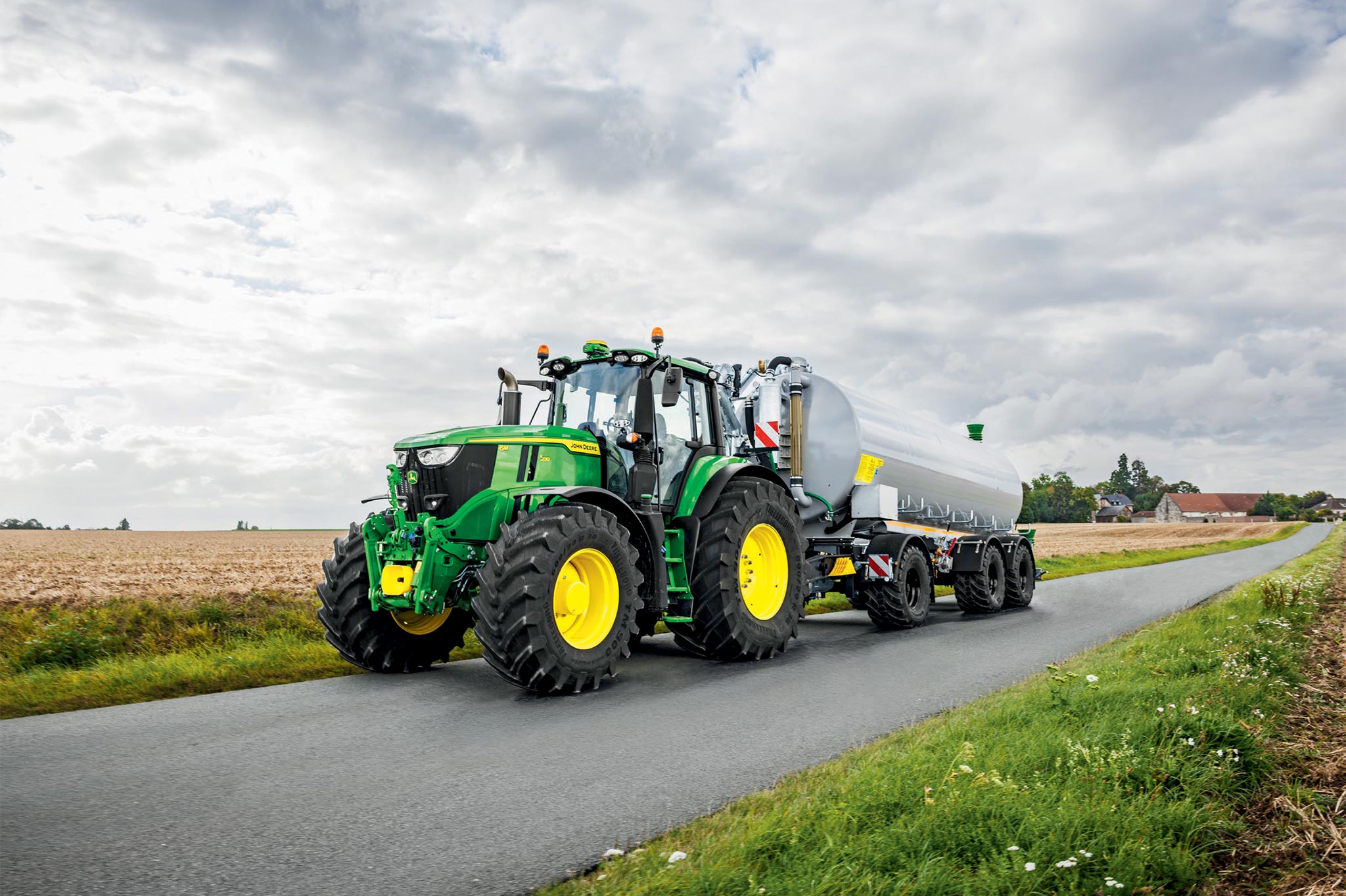 Un tracteur John&nbsp;Deere de la série 6M travaillant dans un champ moissonné à l’aide de cultivateurs à dents larges, vu d’en haut avec un nuage de poussière qui s’élève.