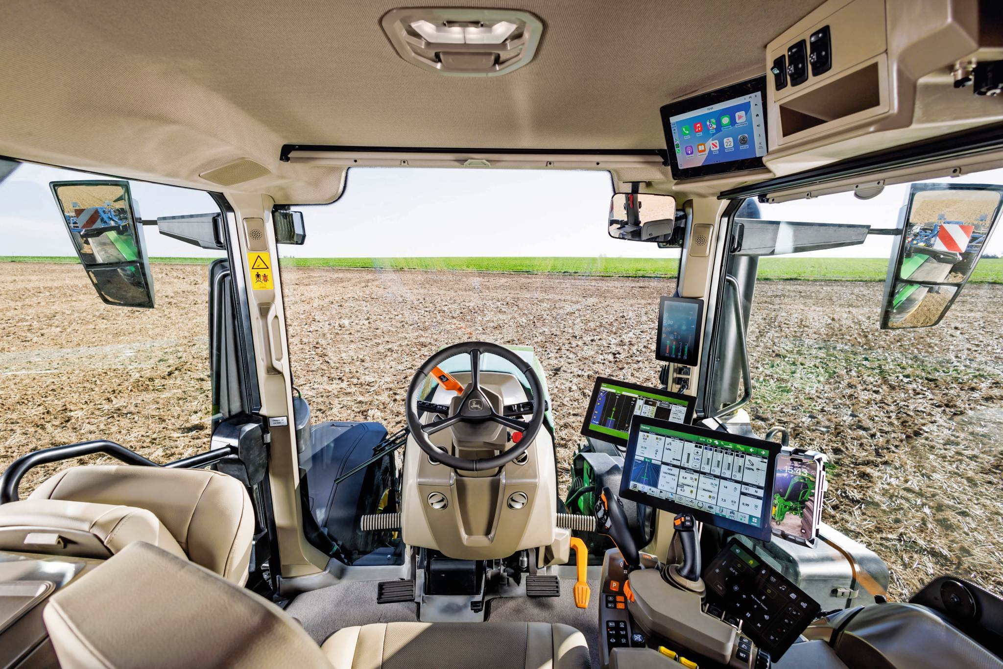 Moderner Innenraum einer Traktorkabine mit Lenkrad, Touchscreen-Displays und Bedienelementen für die Präzisionslandwirtschaft mit Blick auf ein bewirtschaftetes Feld