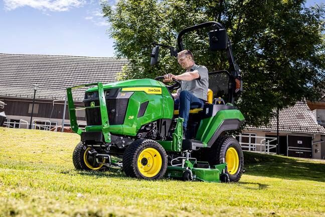 Fahrer, der mit einem John Deere Kompakttraktor und einem Zwischenachsmähwerk einen Grashang mäht