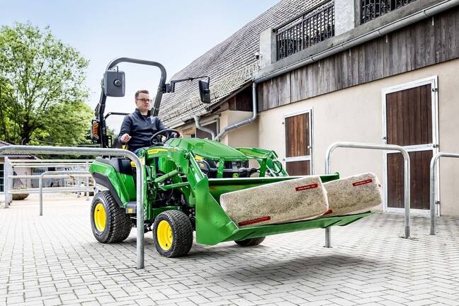 John Deere Kompakttraktor mit zwei Einstreuballen in einer Frontladerschaufel